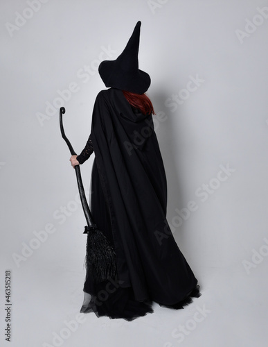 Fotografie Full length portrait of dark haired woman wearing  black victorian witch costume with  cloak and pointy hat