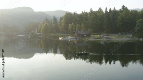 Fisherman On Boat Floating At Lake Bohinj On Bright Sunny Day With Reflections On Tranquil Water. - aerial photo