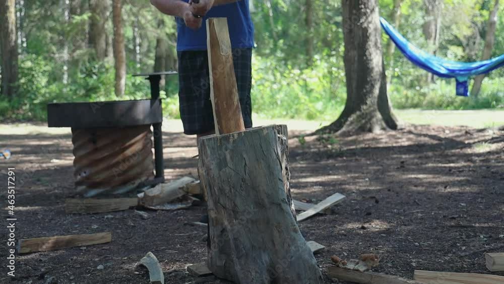 Slow motion, man chopping wood in half on tree trunk while camping. Low angle no face Slow motion, man chopping wood in half on tree trunk while camping. Low angle no face