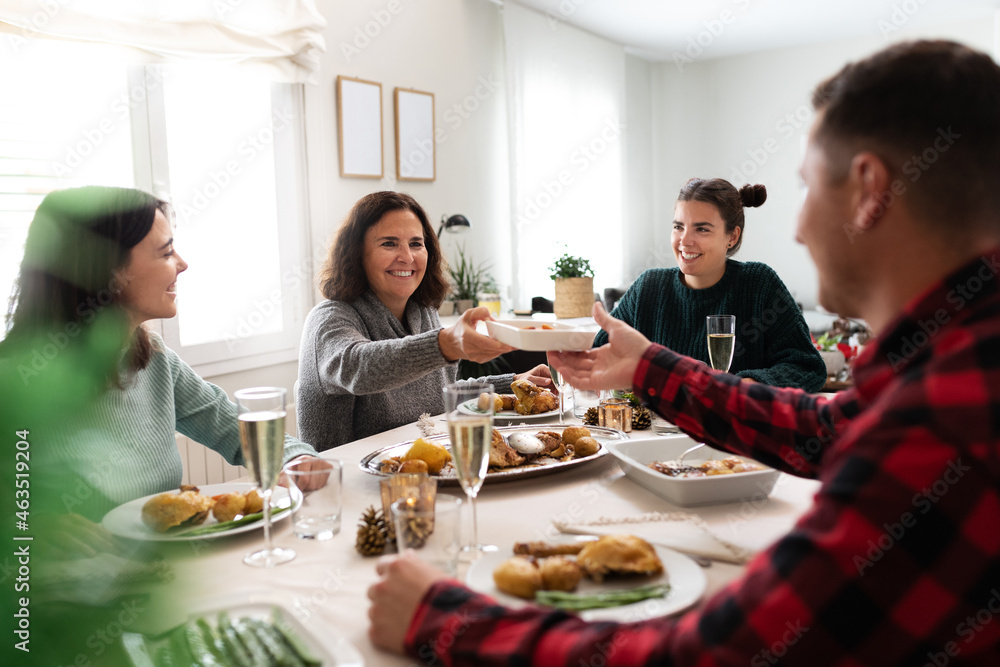 Mature caucasian woman pass plate of food to young man during family Christmas dinner.
