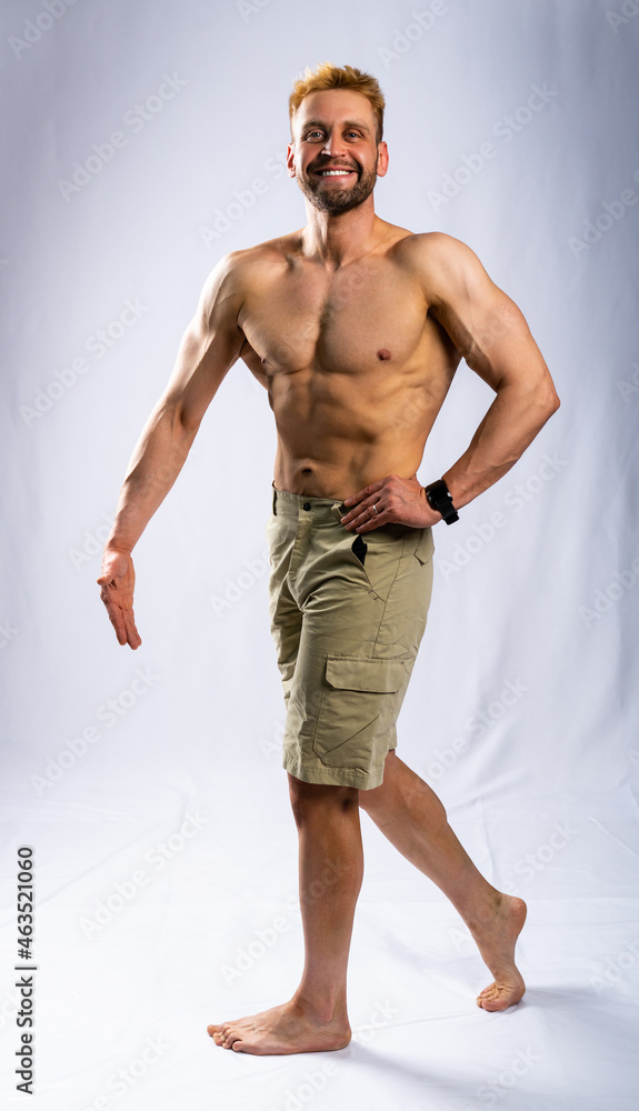 muscular man in shorts posing, shows, straining muscles. gray background