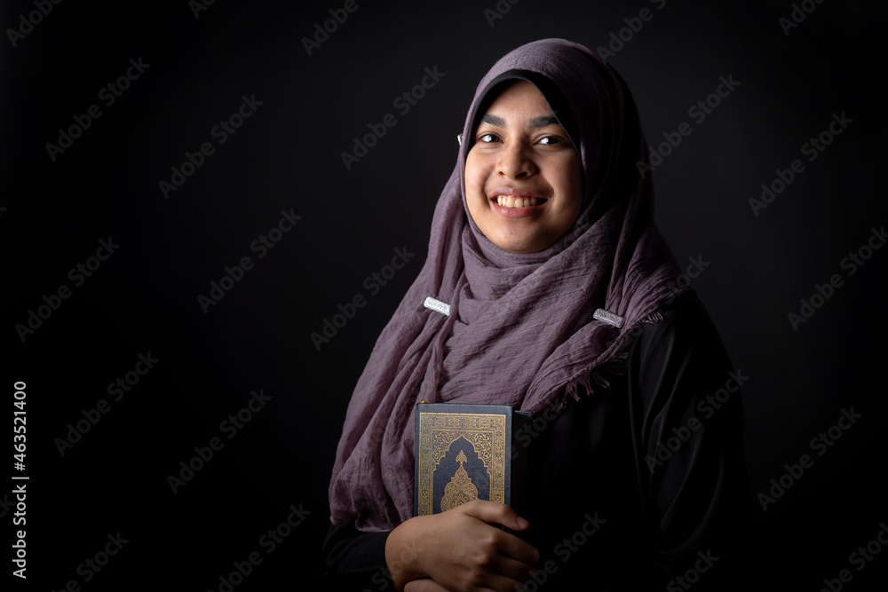 Portrait Asian Muslim woman standing and reading the Quran and appreciates and faith The Holy Al Quran with written Arabic calligraphy meaning of Al Quran, Arabic word translation: The Holy Al Quran. Portrait Asian Muslim woman standing and reading the Quran and appreciates and faith The Holy Al Quran with written Arabic calligraphy meaning of Al Quran, Arabic word translation: The Holy Al Quran.
