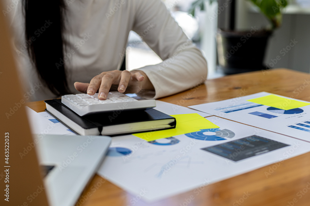 A finance worker presses a calculator to verify the accuracy of the company's financial data on a laptop, she prepares a company financial summary to bring to a meeting with the management. A finance worker presses a calculator to verify the accuracy of the company's financial data on a laptop, she prepares a company financial summary to bring to a meeting with the management.