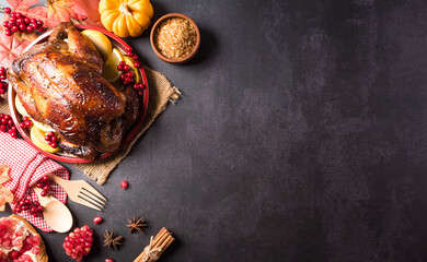 Thanksgiving dinner background concept with turkey roasted and all sides dishes, fall leaves, pumpkin and seasonal autumnal decor on dark stone background, top view, copy space.