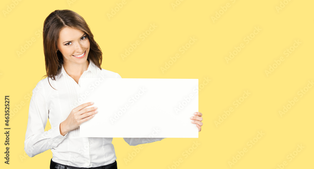 Happy smiling woman in white confident wear holding showing mock up empty signboard. Businesswoman in advertising studio concept. Copy space area. Yellow color background.. Happy smiling woman in white confident wear holding showing mock up empty signboard. Businesswoman in advertising studio concept. Copy space area. Yellow color background..