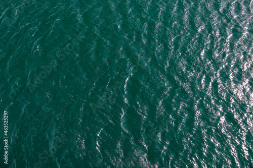 bewegte Wasseroberfläche mit Wellen und Gischt eines Sees im Sonnenlicht von oben