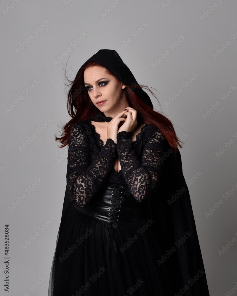 close up portrait of red haired woman wearing black victorian witch costume. standing pose, with gestural hand movements, against dark studio background. close up portrait of red haired woman wearing black victorian witch costume. standing pose, with gestural hand movements, against dark studio background.