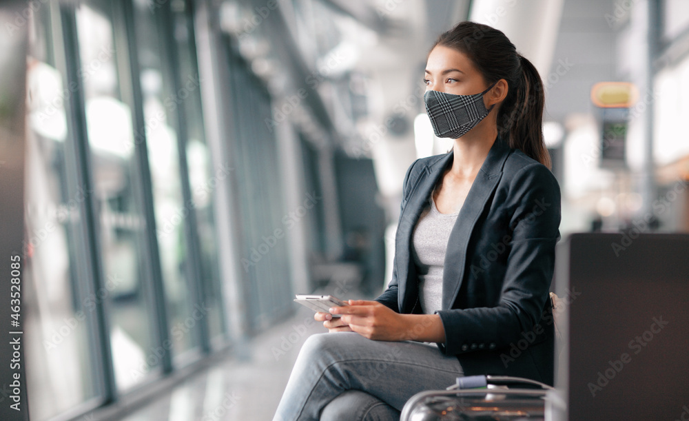 Travel during coronavirus. Asian business woman wearing face mask in airport terminal waiting for flight thinking looking out the window using phone app for vaccine passport. - obrazy, fototapety, plakaty 