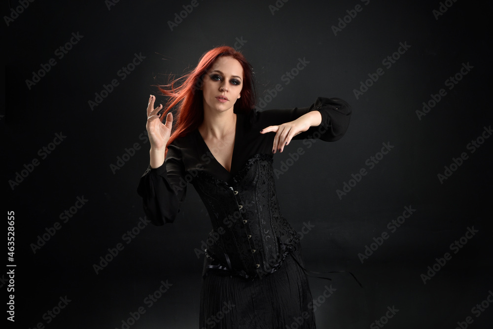 close up portrait of red haired woman wearing black victorian witch costume. standing pose, with gestural hand movements, against dark studio background. close up portrait of red haired woman wearing black victorian witch costume. standing pose, with gestural hand movements, against dark studio background.