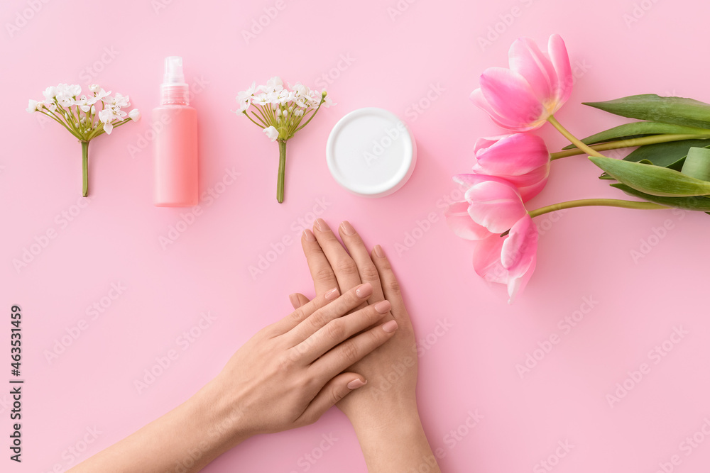 Female hands with cosmetic products and flowers on color background