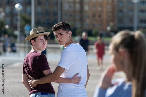 Gay angry teenager couple looking back to surprised woman. Homophobia in adolescence concept. photo