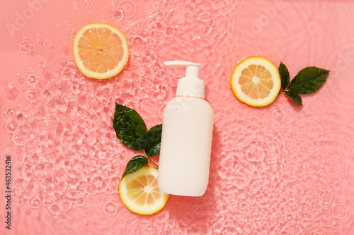 Bottle of cosmetic product with orange and leaves in water on color background