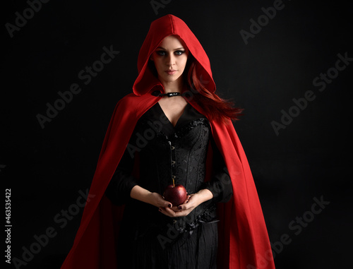 фотографія close up portrait of girl wearing red riding hood cloak and witch costume, isolated on black studio background with shadowy  rim lighting
