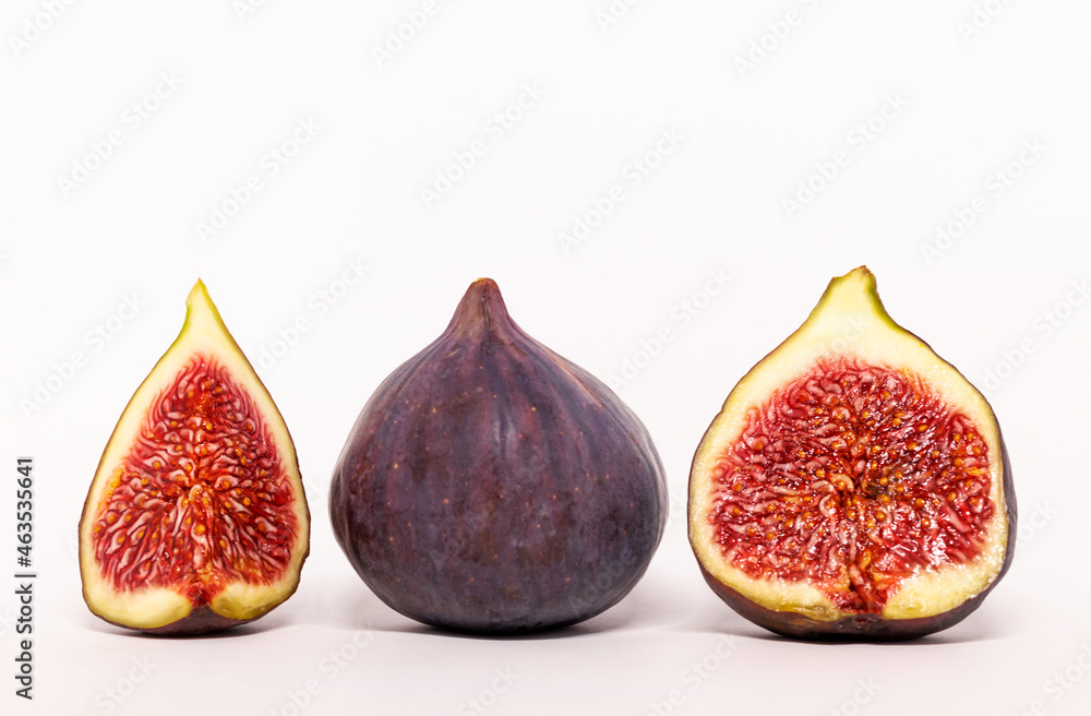 Ripe figs and half a fruit on a green leaf background. Fresh fruit. White background. Ripe figs and half a fruit on a green leaf background. Fresh fruit. White background.