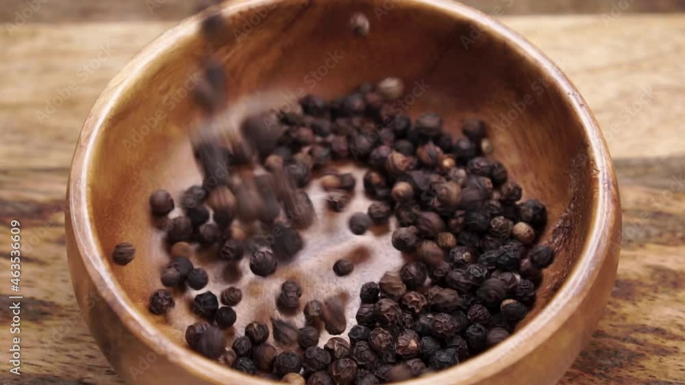 Black dry peppercorn falling into a wooden rustic bowl on a wood table in slow motion close up Black dry peppercorn falling into a wooden rustic bowl on a wood table in slow motion close up