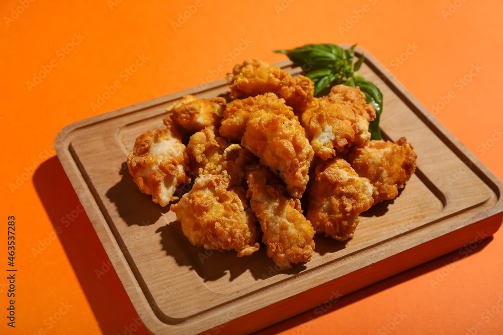 Board with tasty fried popcorn chicken on orange background Board with tasty fried popcorn chicken on orange background