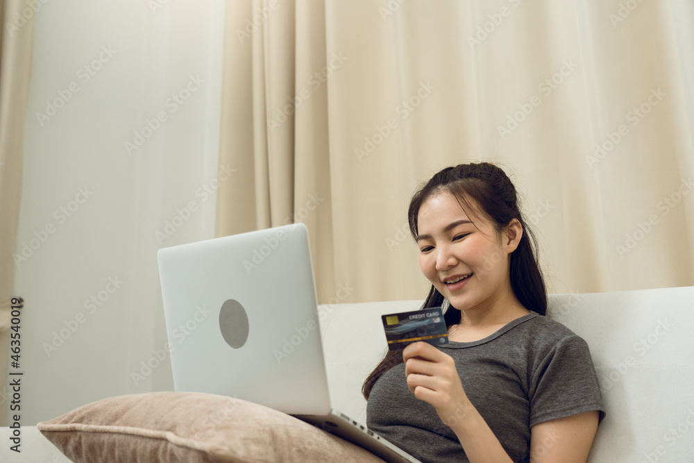 Asian woman holding a credit card for online shopping while sitting on the couch while on vacation at home. Asian woman holding a credit card for online shopping while sitting on the couch while on vacation at home.