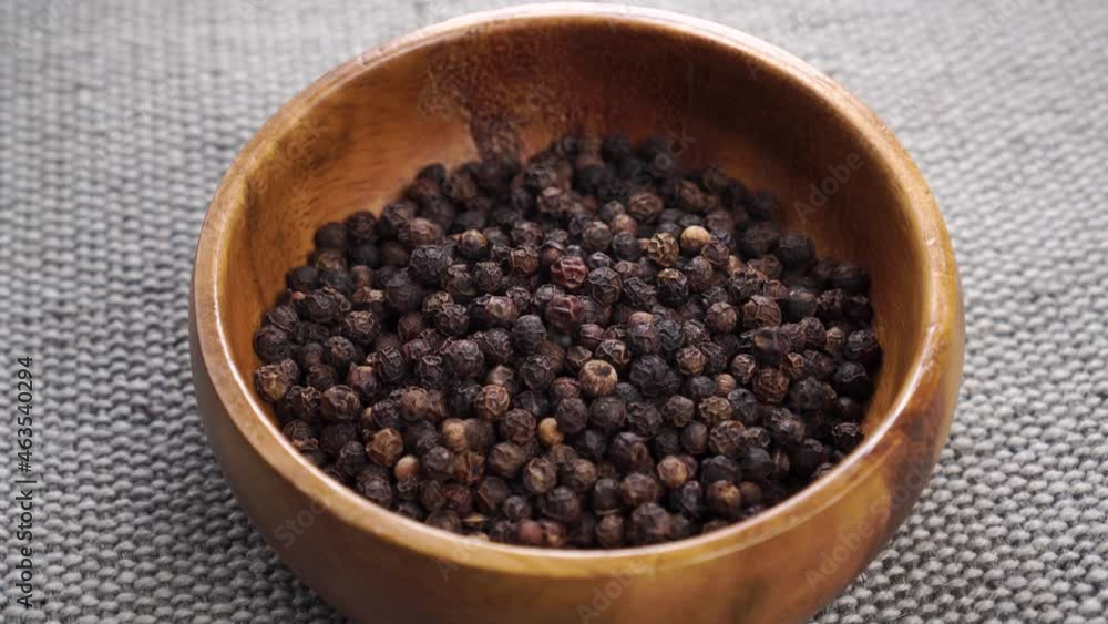 Dried black pepper grains fall into a wooden bowl on a jute burlap in slow motion. Close up. Spice and seasoning. Dry peppercorns Dried black pepper grains fall into a wooden bowl on a jute burlap in slow motion. Close up. Spice and seasoning. Dry peppercorns