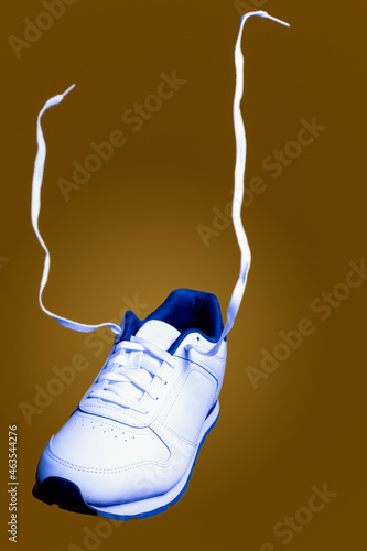 One Isolated New White Sneaker With Lifted Soaring Shoelaces Over Colorful Yellow Background.