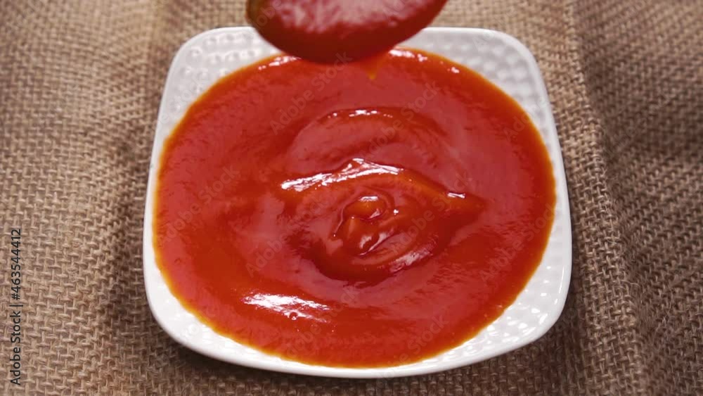 Dripping fresh tomato sauce from spoon into a white saucer. On a rough rustic cloth. Slow motion. Close up. Red ketchup, vegetable paste Dripping fresh tomato sauce from spoon into a white saucer. On a rough rustic cloth. Slow motion. Close up. Red ketchup, vegetable paste