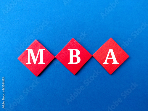 Colored wooden cube written with text MBA on blue background.