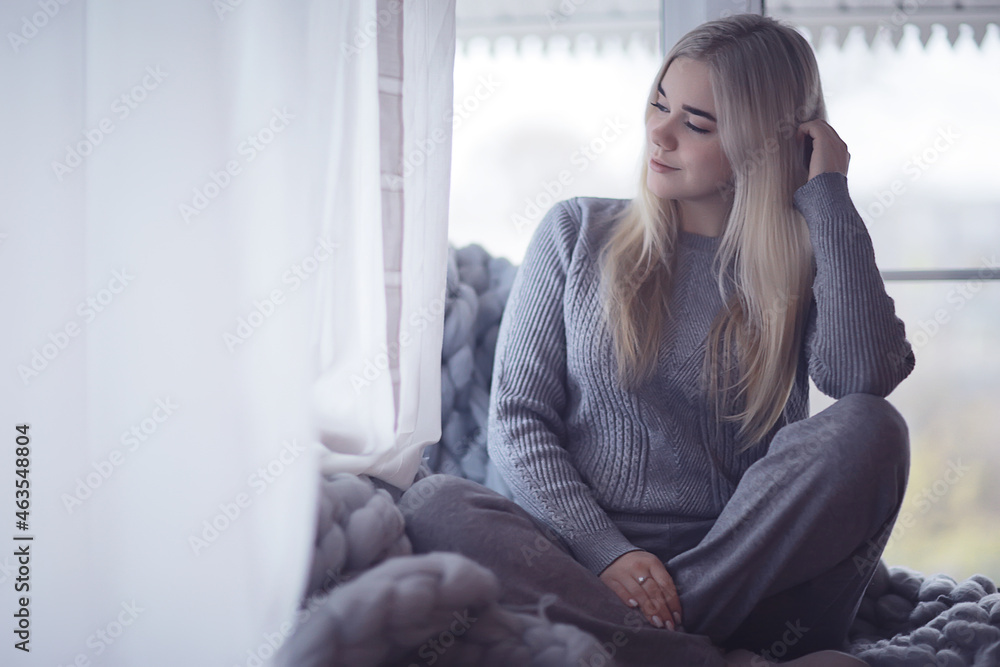 winter home interior, model girl basking in a knitted blanket at the window, a cold day at home winter home interior, model girl basking in a knitted blanket at the window, a cold day at home