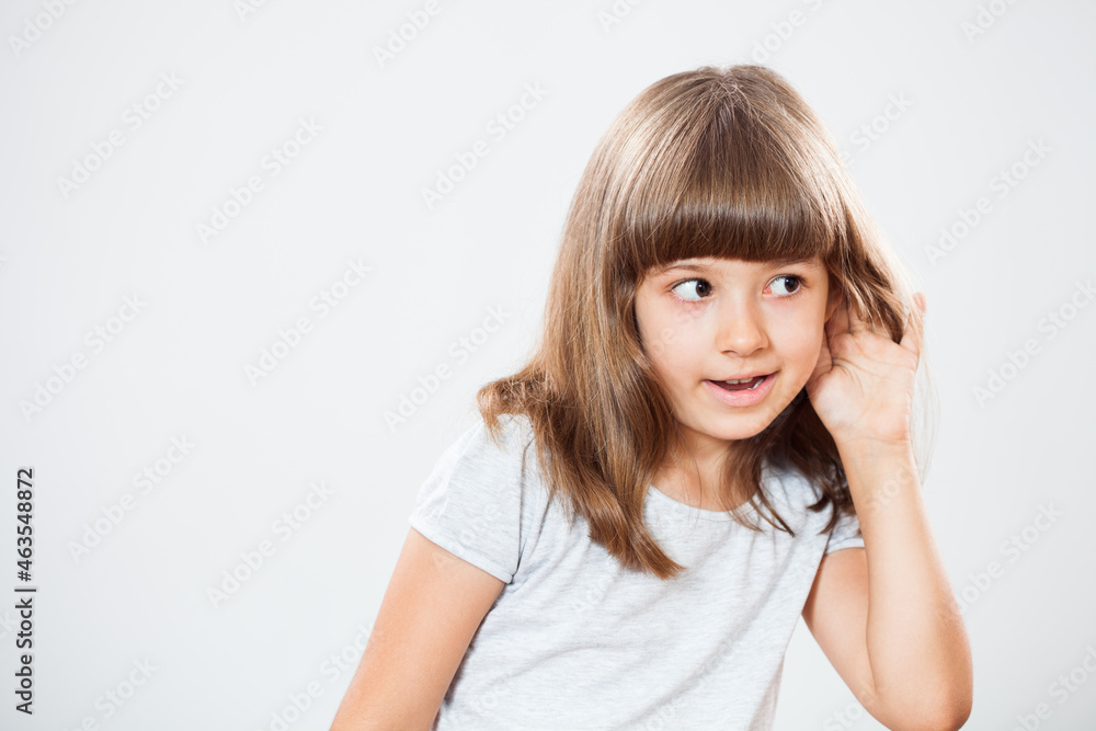 Studio shot portrait of thoughtful little girl who is eavesdropping. Copy space on gray background. Studio shot portrait of thoughtful little girl who is eavesdropping. Copy space on gray background.
