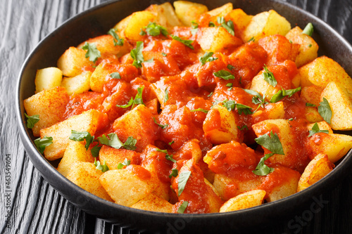 Spanish Crispy fried potatoes tossed in spicy brava sauce close up in the plate on the table. Horizontal