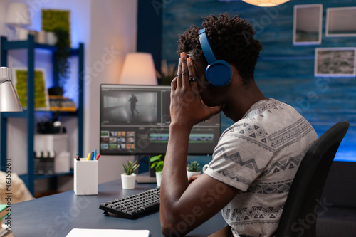 African american editor retouching film montage using editing post production sofware working at visual effects for multimedia project. Young videographer sitting at desk looking at digital movie
