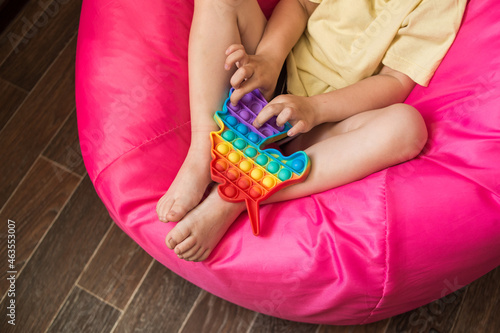 A little girl is playing with a modern pop it toy unicorn. A fascinating sensory toy for the development of hand motor skills. Colorful popit toy.Simple dimple. Baby's bare feet close up