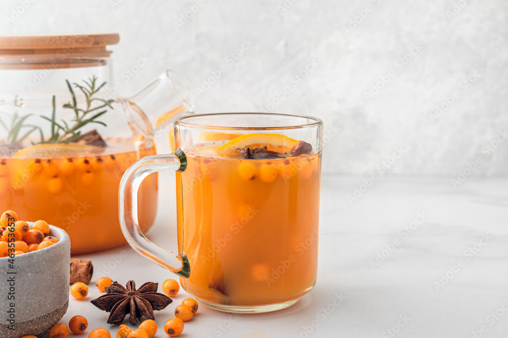 Sea buckthorn autumn tea with orange in glass cup and teapot with fresh berries, cinnamon and rosemary on white table Sea buckthorn autumn tea with orange in glass cup and teapot with fresh berries, cinnamon and rosemary on white table