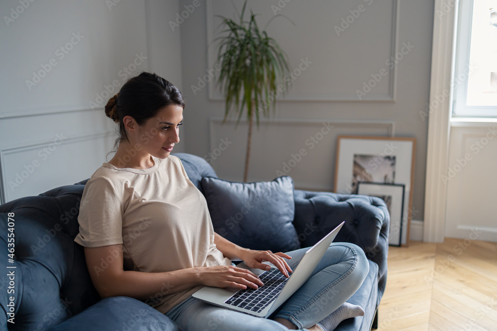 Young woman using computer on sofa in the living room. Young woman using computer on sofa in the living room.