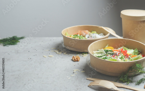 Healthy lunch in eco-friendly packaging with wooden cutlery. Plastic free take away food on grey kitchen table at grey wall background. Modern sustainable food delivery. Front view with copy space.