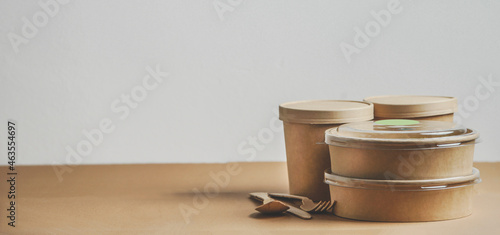 Selection of modern sustainable food delivery containers and cutlery on kitchen table at white wall background. Front view with copy space. Banner
