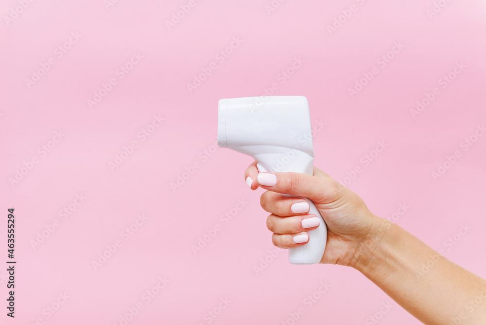 Woman's hand holding white thermometer on pink background Woman's hand holding white thermometer on pink background