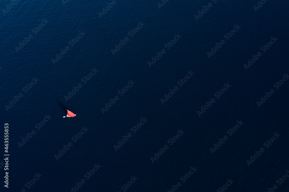 View from above, stunning aerial view of a sailboat with a red sail sailing on a blue water during a sunny day, Sardinia, Italy.