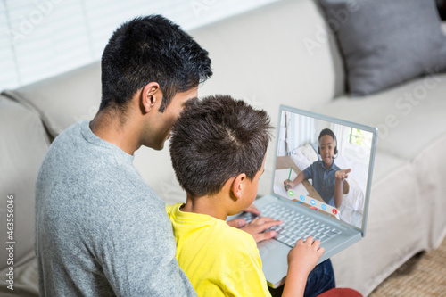 Biracial boy with father using laptop for video call, with elementary school pupil on screen