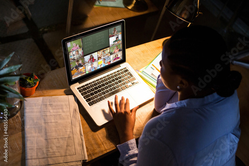 African american woman using laptop for video call, with diverse elementary school pupils on screen