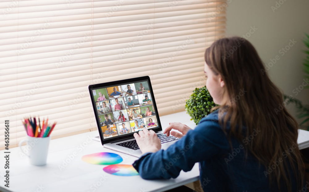 Obraz premium Caucasian girl using laptop for video call, with smiling diverse elementary school pupils on screen