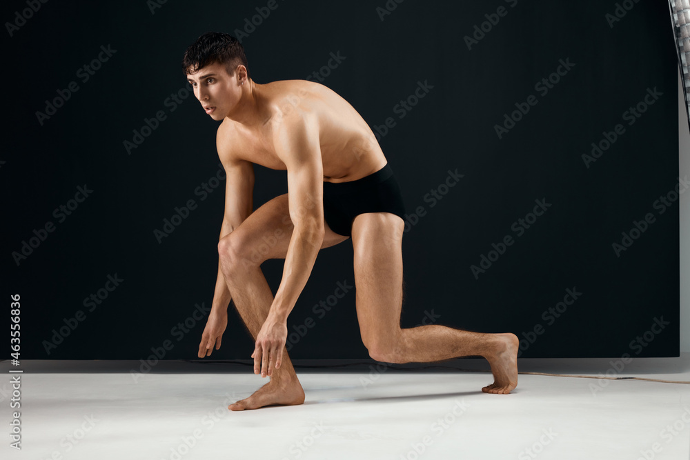 athletic man in black shorts with a muscular body stands on his knee dark background