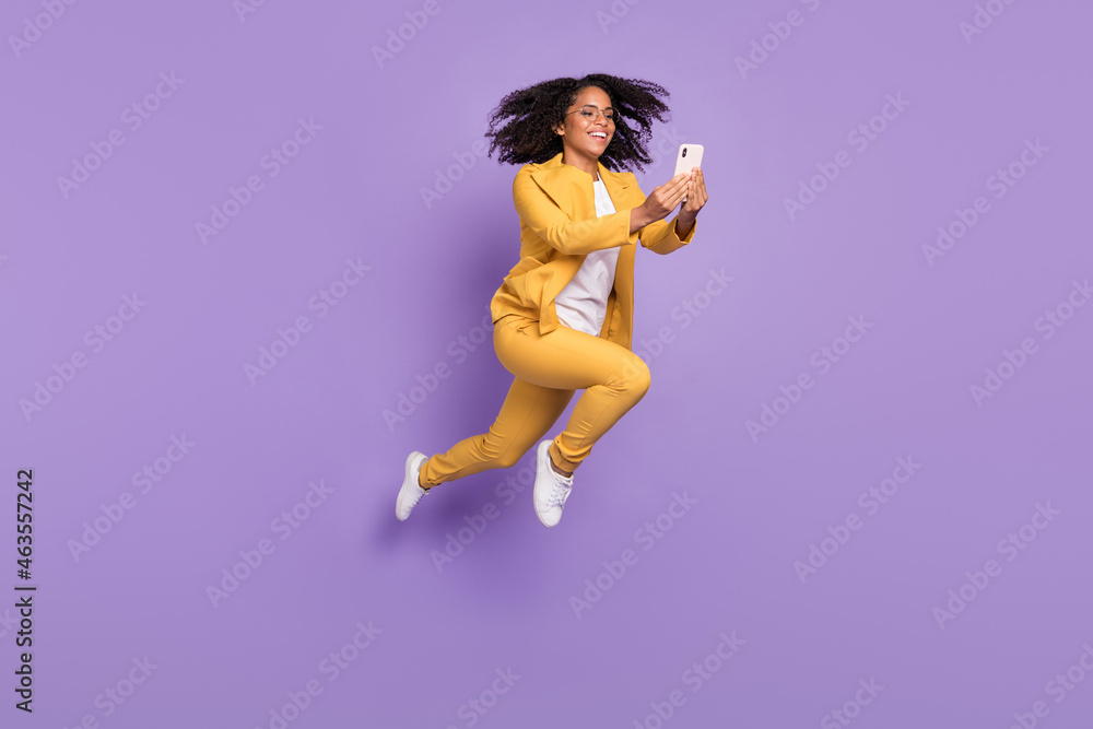 Photo of charming pretty woman dressed yellow suit spectacles jumping typing modern device isolated violet color background