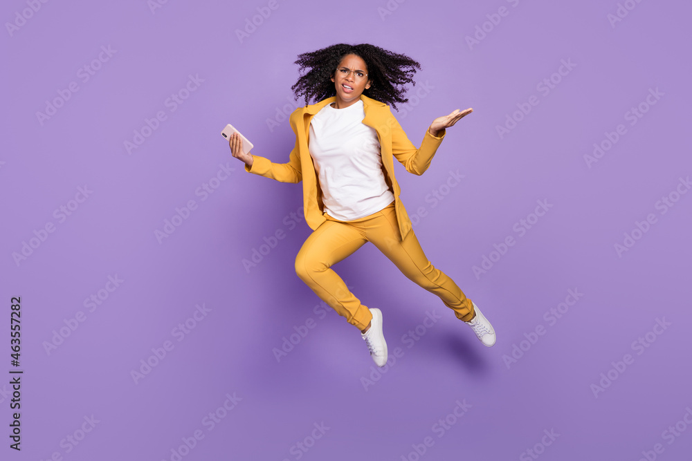 Photo of pretty doubtful woman dressed suit spectacles jumping typing device shrugging isolated violet color background Photo of pretty doubtful woman dressed suit spectacles jumping typing device shrugging isolated violet color background