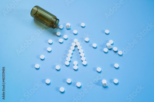 White medical pills and tablets spilling out of a drug bottle on a blue background. Christmas theme, pills like a Christmas tree. So boxes as an arrow