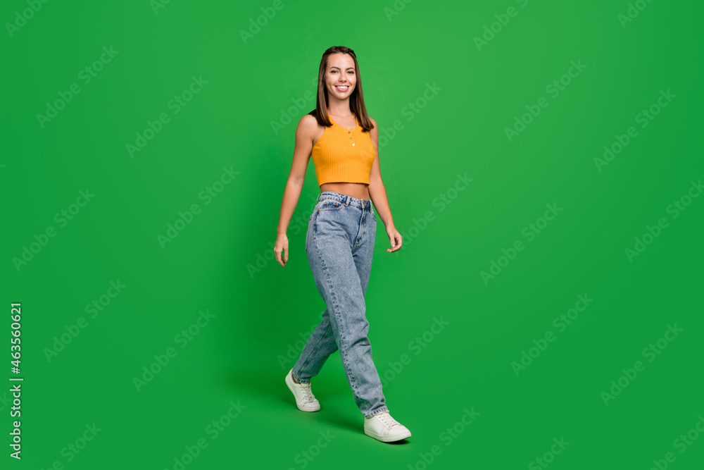 Full size photo of funny millennial brunette lady go wear top jeans sneakers isolated on green color background Full size photo of funny millennial brunette lady go wear top jeans sneakers isolated on green color background