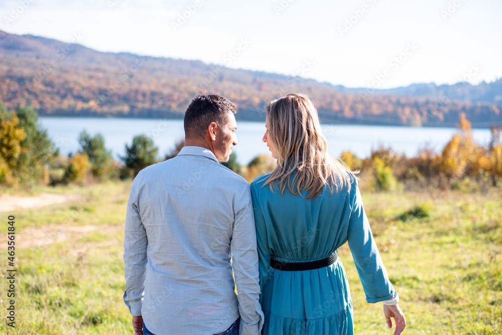 Couple stay by back on background lake with mountain in autumn forest. Autumn has painted foliage on trees with yellow colours. romantic place. love between man and woman.
