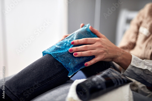 Woman with spasm, cramp, sprained, dislocated knee, ruptured tendon and joint pain, using cold gel pack at home. photo