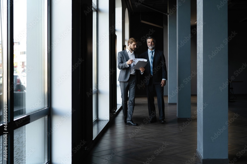 Two colleagues communicating in corridor, partners walking in the modern office Two colleagues communicating in corridor, partners walking in the modern office