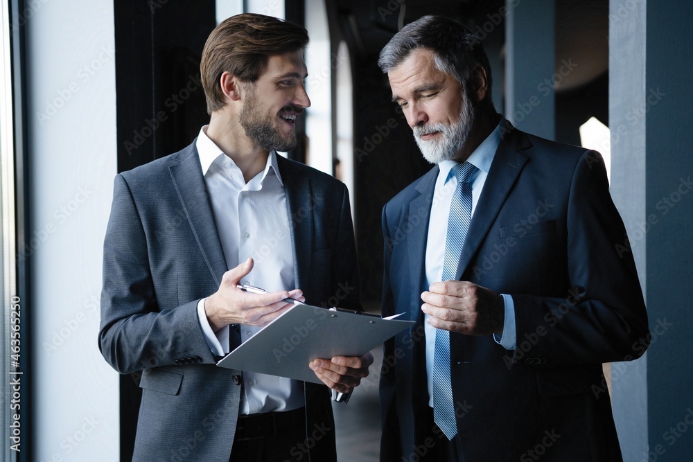 © opolja - Two colleagues communicating in corridor, partners walking in the modern office