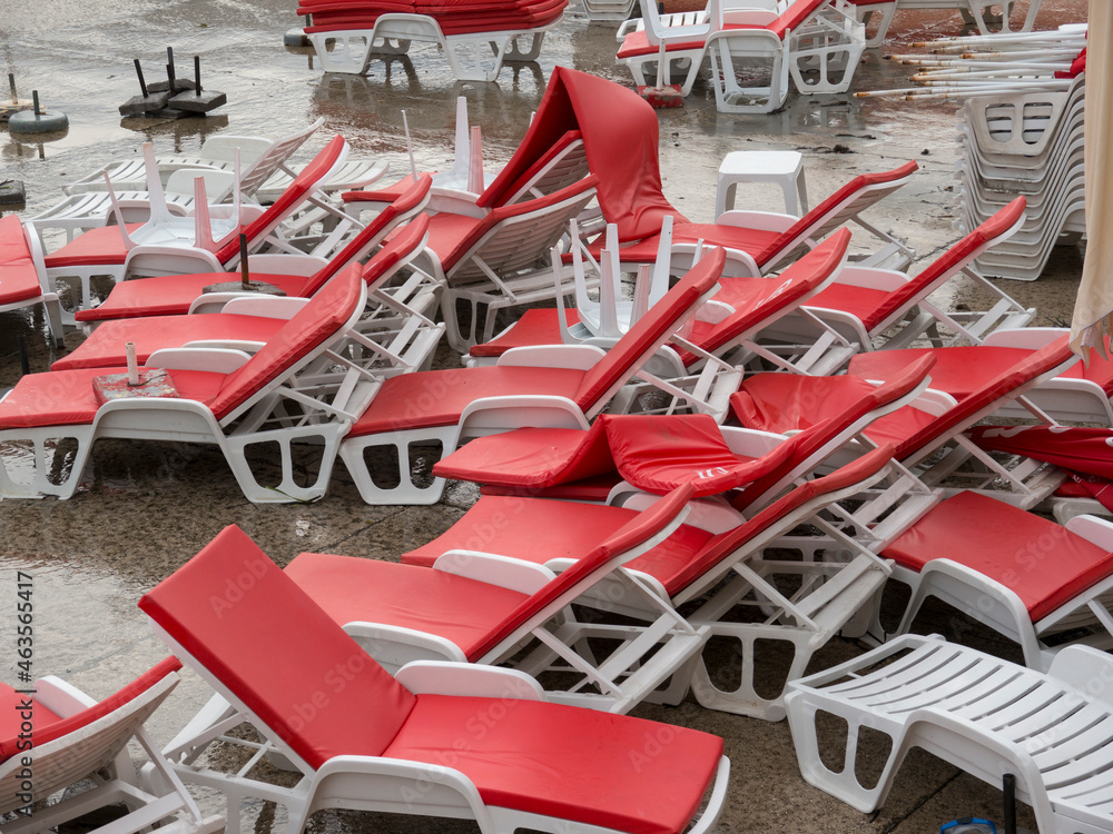 Heap of white plastic chaise lounge with red mattresses and sunshades on sea side cement beach top view