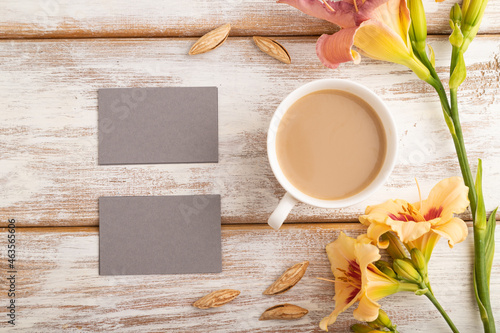 Gray paper business card mockup with orange day-lily flower and cup of coffee on white wooden background. top view, copy space.